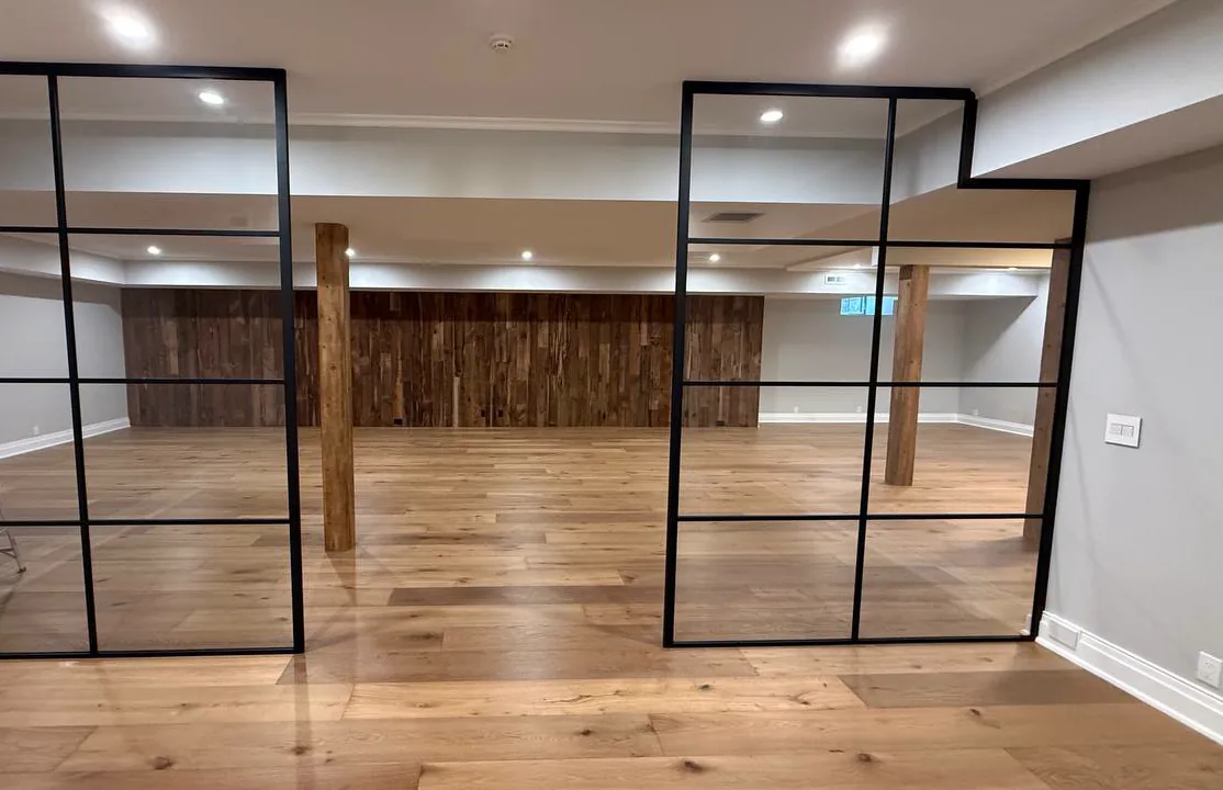 Two glass partition panels notched around a stepped-down ceiling soffit in a Connecticut lower level, by WiseGlass NY