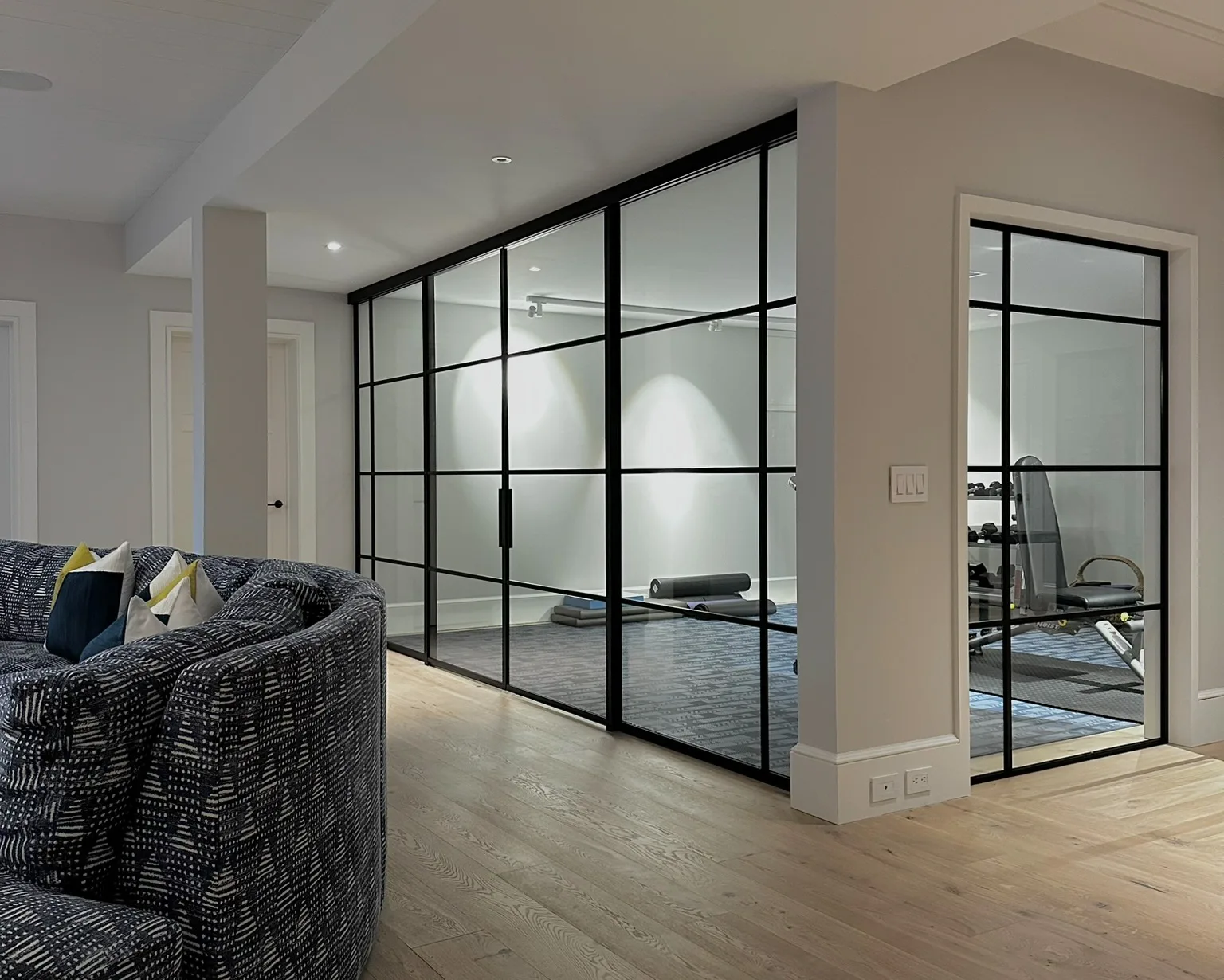 Double-sliding black matte powder-coated aluminum-framed glass partition enclosing a residential gym, Sagaponack NY by WiseGlass NY