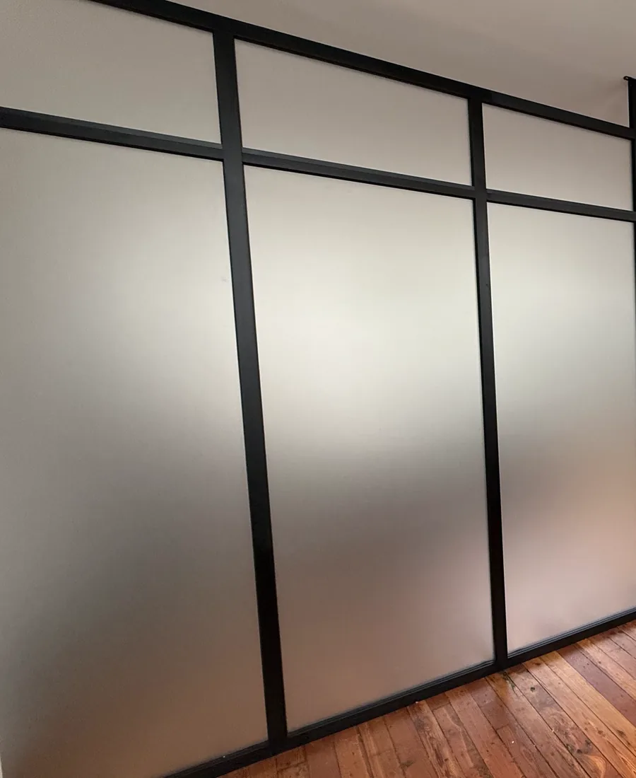 Close view of a frosted glass partition panel glowing with diffused light behind a black matte frame, Manhattan loft by WiseGlass NY
