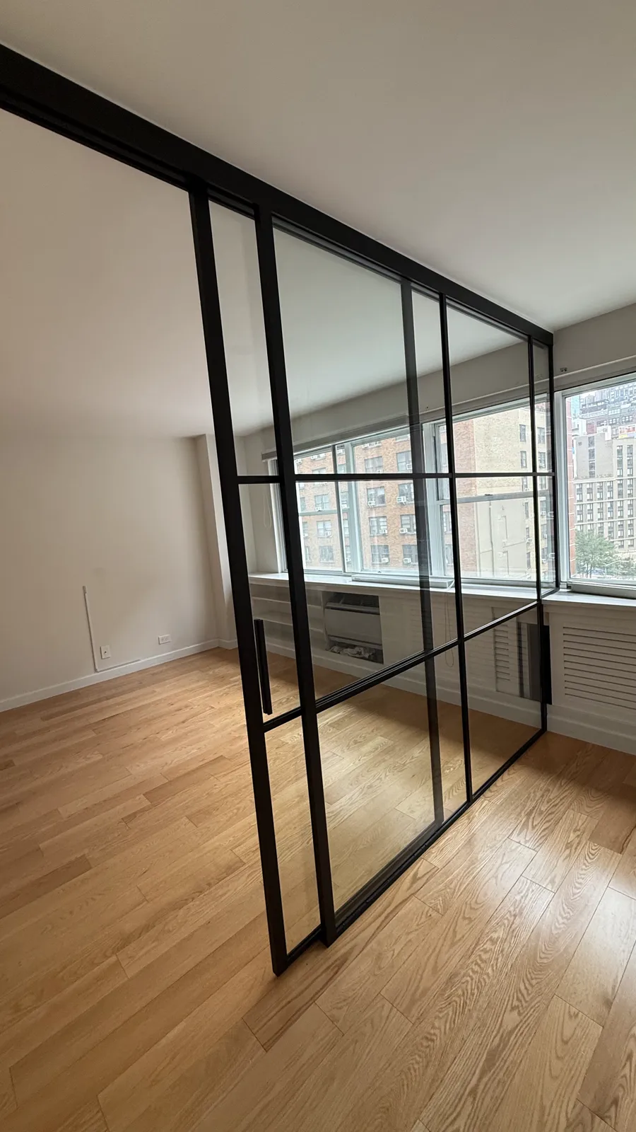 Single sliding glass door open in a black-framed partition with a step up over a radiator enclosure, Manhattan by WiseGlass NY
