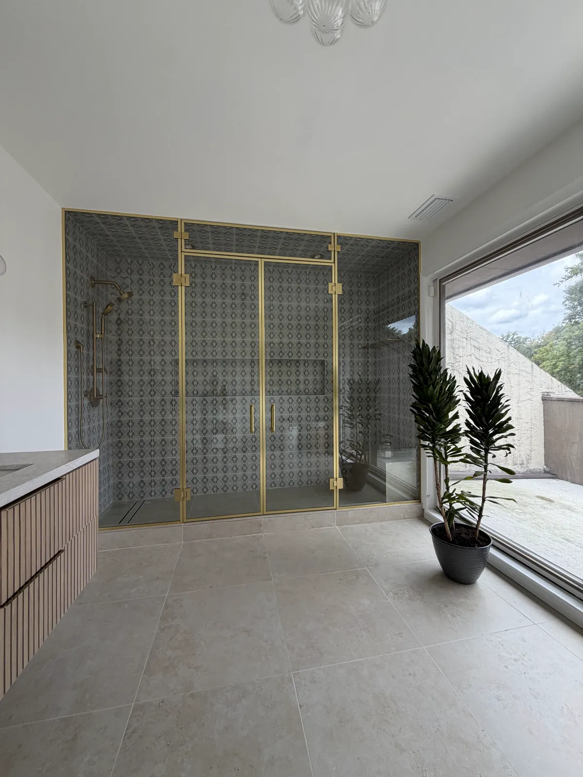 Walk-in shower closed by brass-framed glass French doors with a glass transom above, West Orange NJ primary bathroom by WiseGlass NY