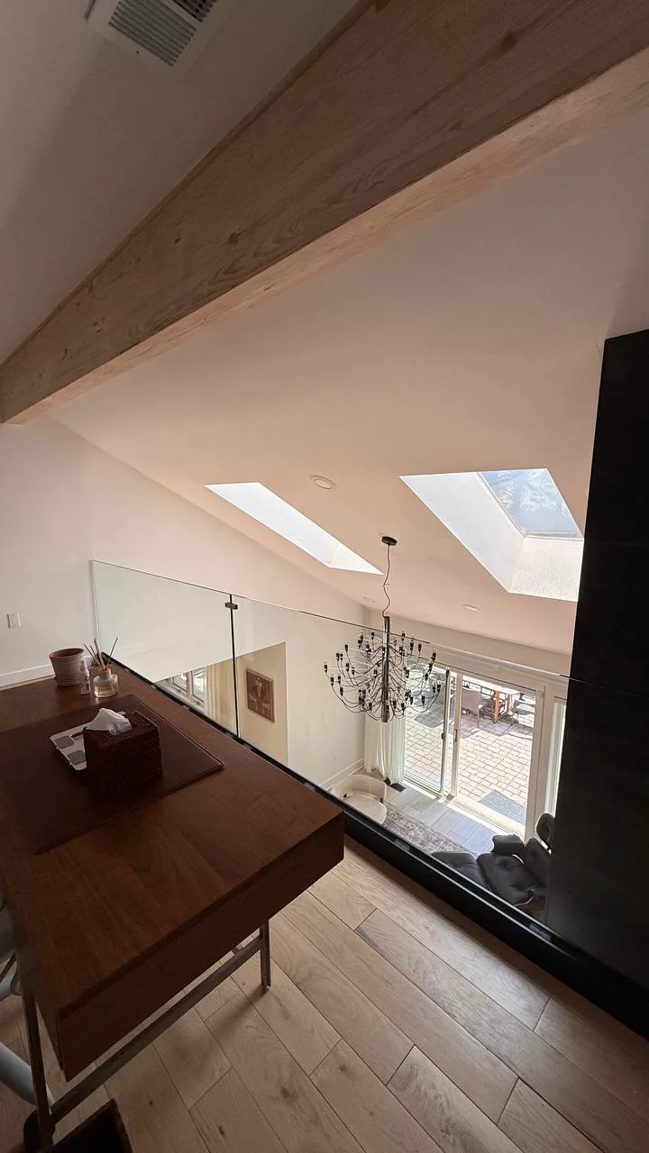 Frameless laminated glass mezzanine railing set in a black base shoe, overlooking a skylit double-height living room in a New York City home by WiseGlass NY