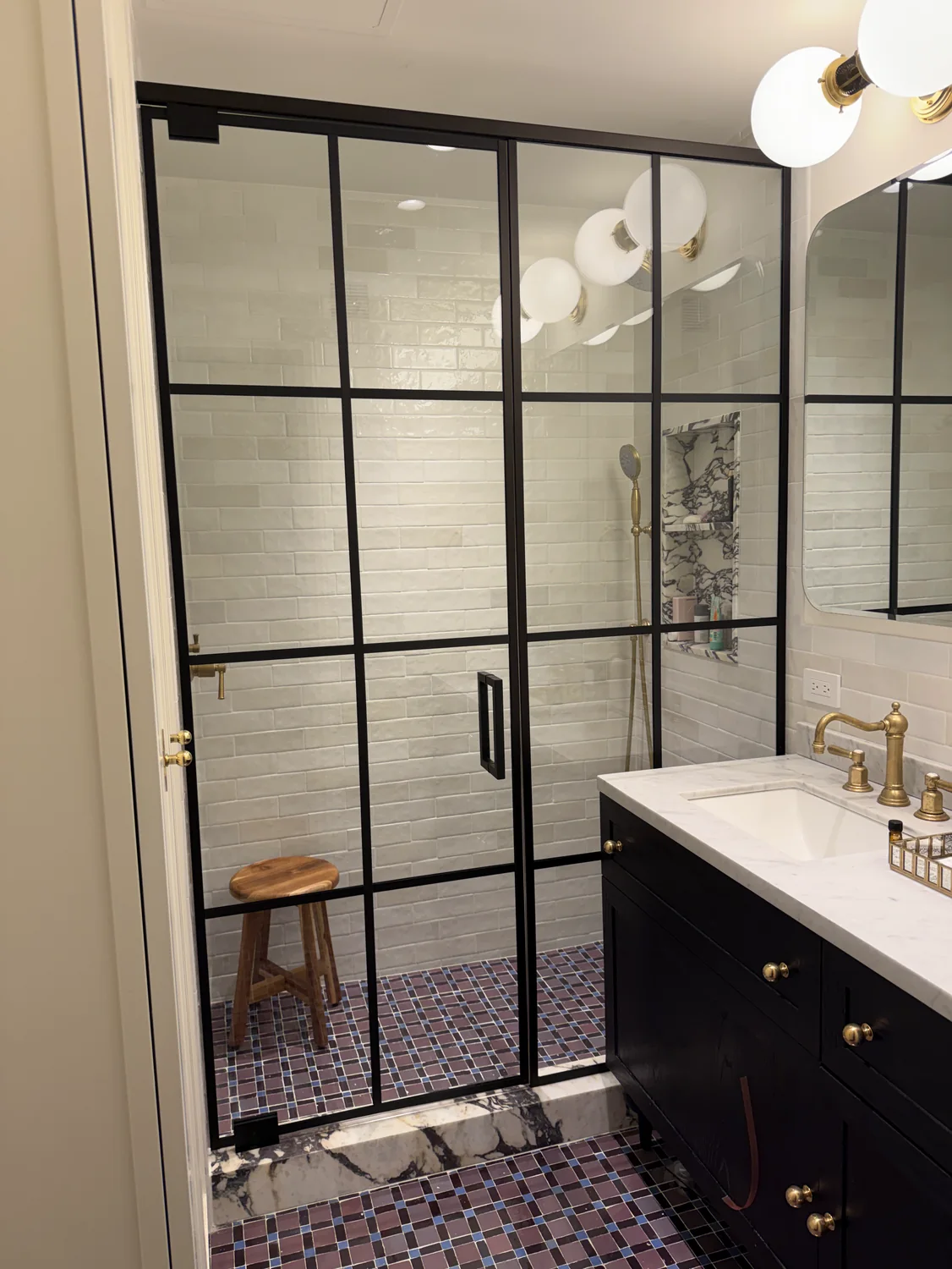 Black grid shower enclosure with divided lites over a marble curb and mosaic floor, Manhattan bathroom by WiseGlass NY