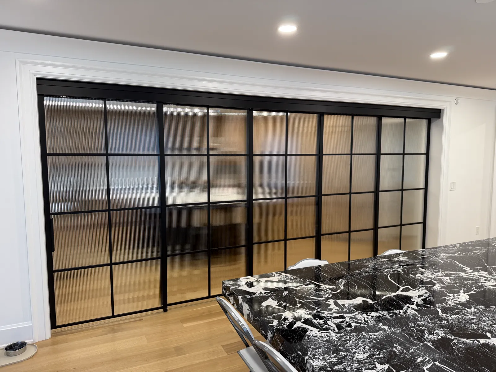 Telescopic sliding wall of black framed reeded glass closed between a kitchen and dining room, Allenhurst NJ by WiseGlass NY