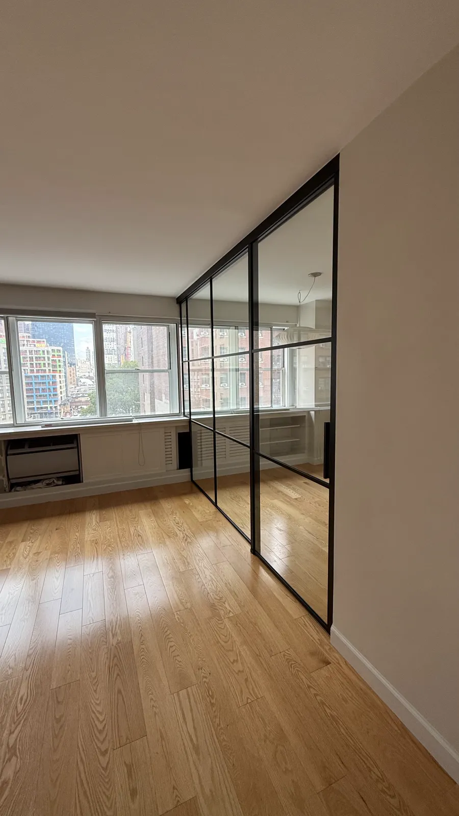 Black framed single sliding glass partition stepping up over a radiator enclosure at the window, Manhattan apartment by WiseGlass NY