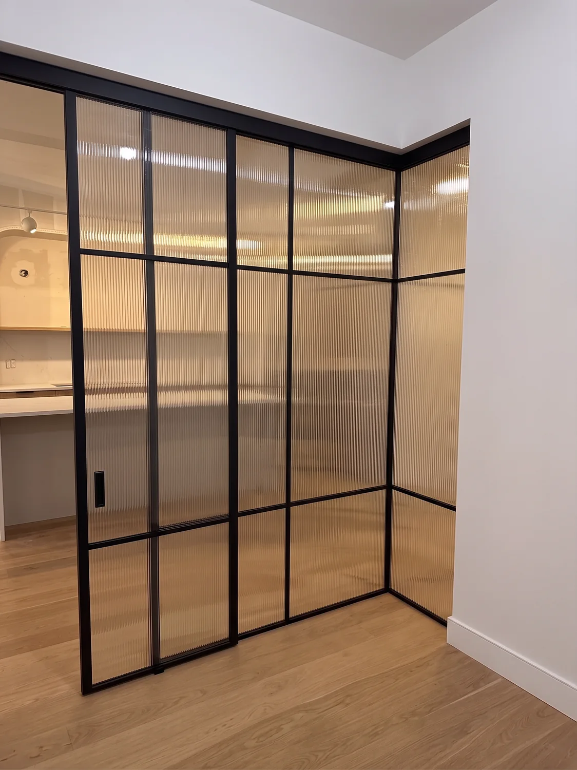 Reeded glass partition return wall with flush recessed pull on the sliding panel, Manhattan by WiseGlass NY